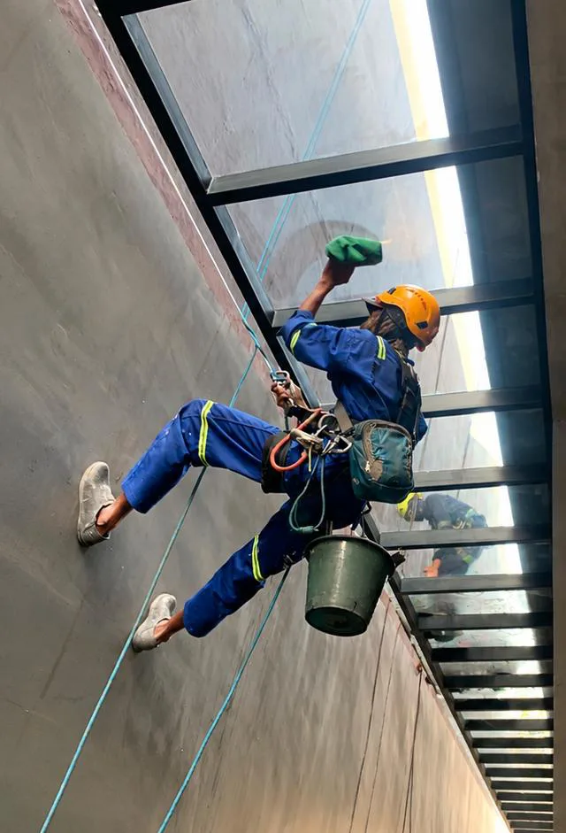 Teknisi rope access membersihkan kaca gedung